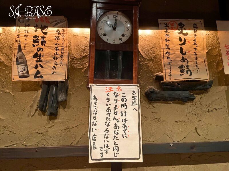 店内の壁に掛けられた古時計と貼り紙。まるげんの温かみあるレトロな雰囲気が漂う。