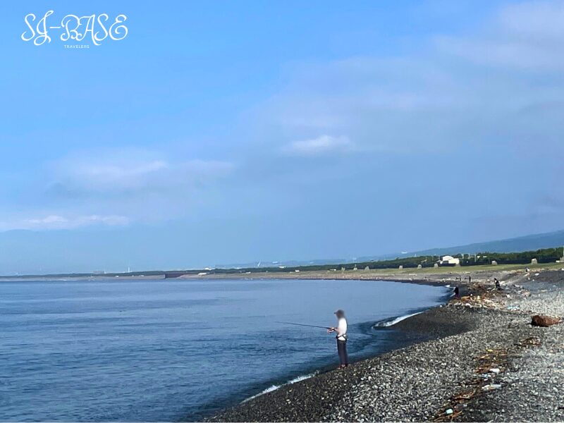 千本浜海岸で竿を出す釣り人。遠くに防波堤と海岸線が見える。