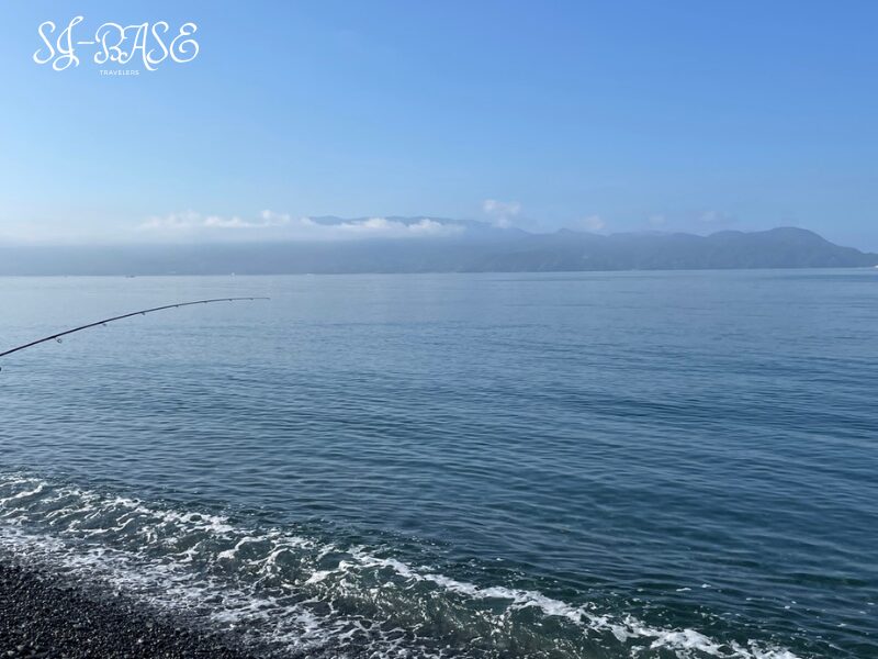 千本浜海岸で釣竿の先が波間に伸びる様子。静かな海面と山並み。
