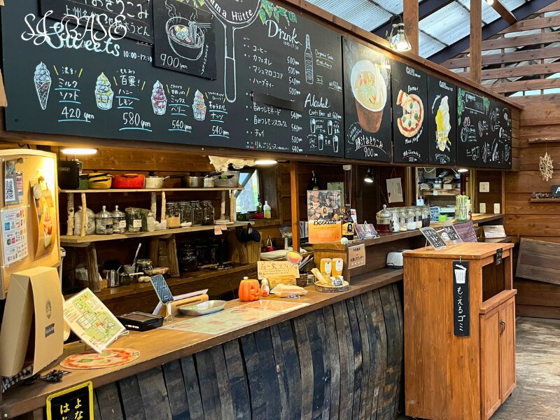 アサマヒュッテのカウンターと黒板メニュー。スイーツやドリンク、ピザなどが並ぶおしゃれな店内。