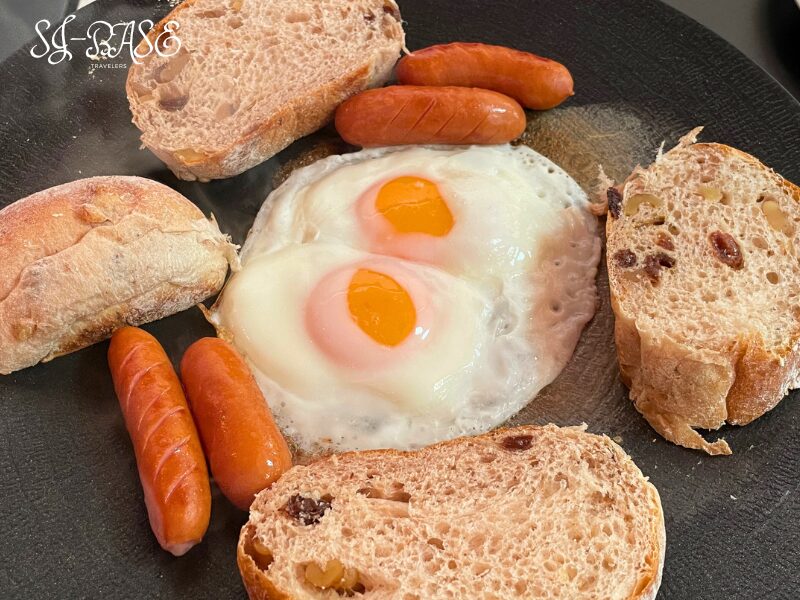 キャンプの朝食プレート。目玉焼きとソーセージ、クルミやレーズン入りのパンを盛り付け。